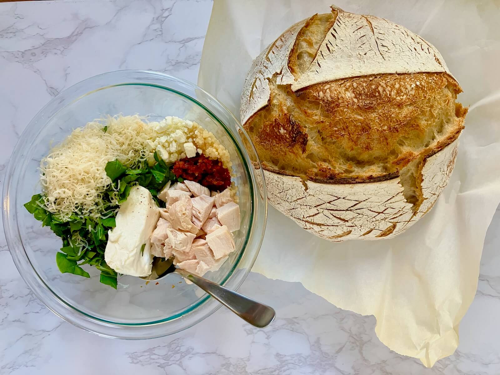 loaf of bread next to a bowl of grilled cheese mixture ingredients such as chicken, sundried tomato and cheese