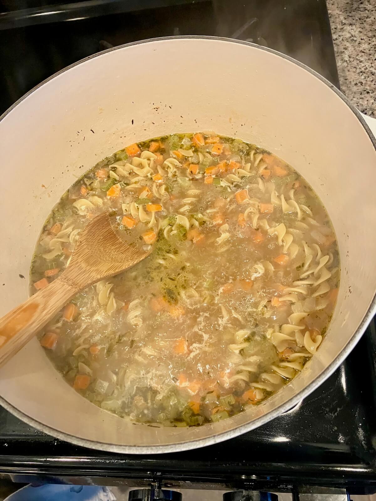 noodles cooking in a pot of broth and vegetables