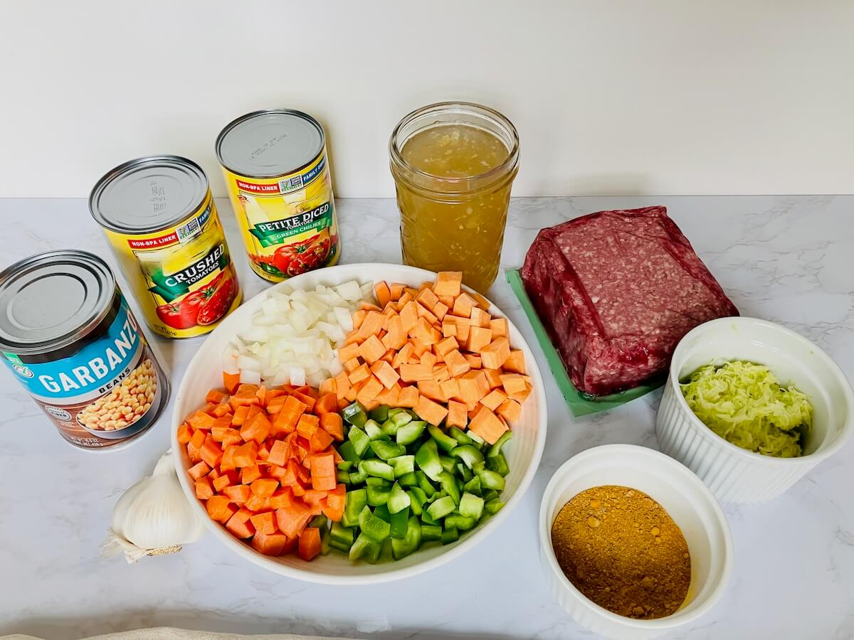 Ingredients for chickpea chili including chickpeas tomato chicken broth garlic chopped vegetables ground beef seasoning and zucchini