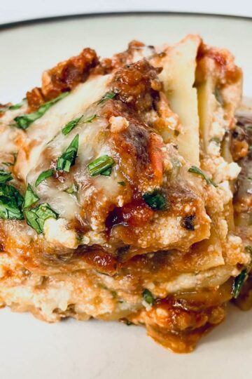 close up of two slices of lasagna stacked on a cream plate