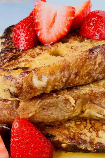 3 sliced of french toast topped with syrup and sliced strawberries