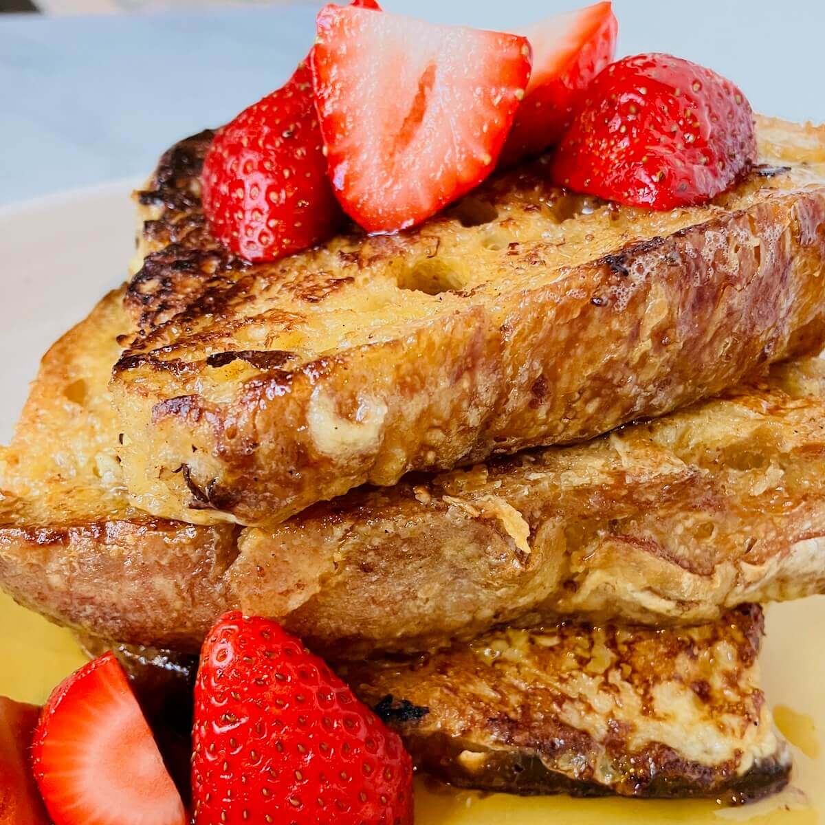 3 sliced of french toast topped with syrup and sliced strawberries