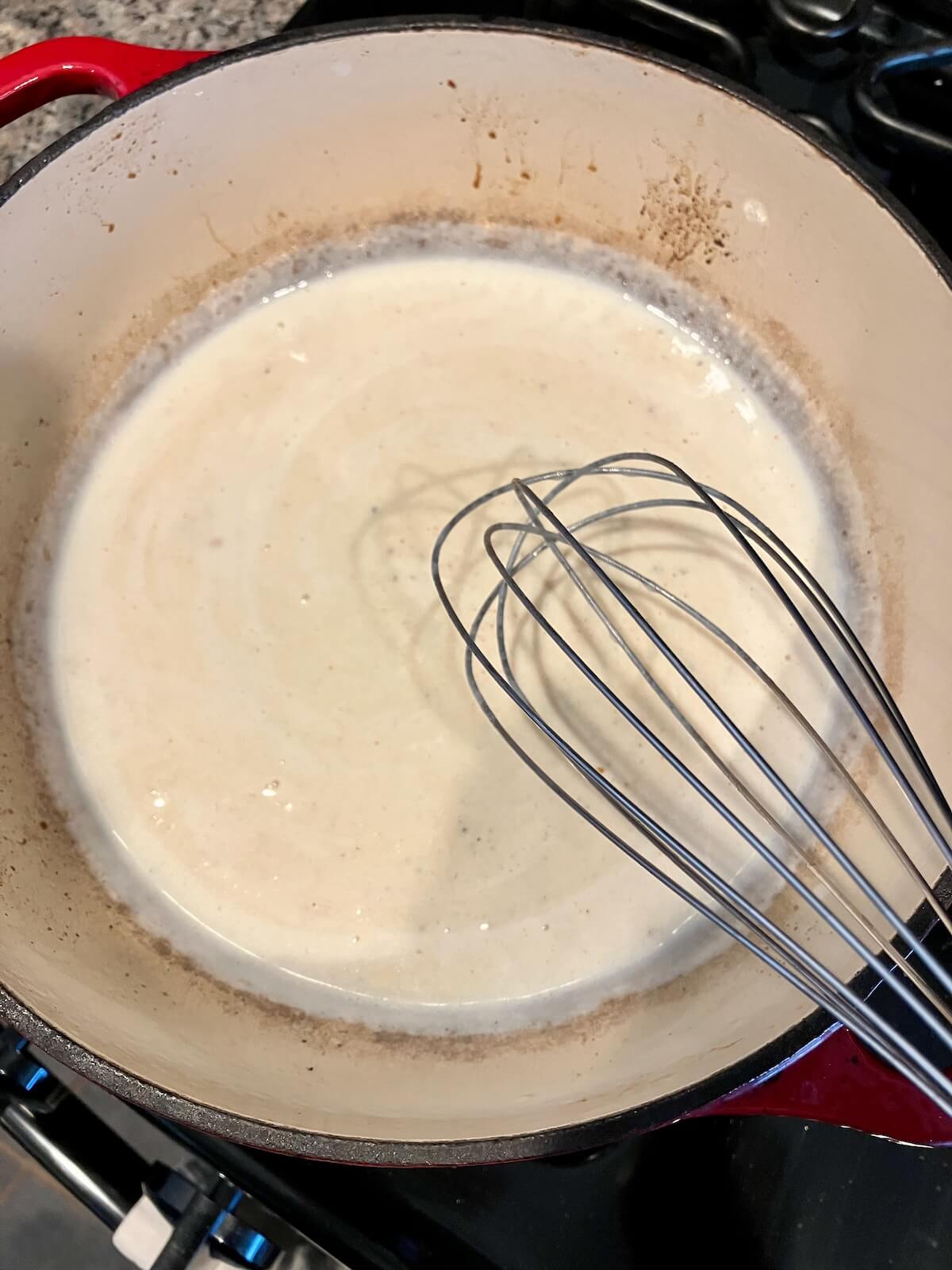 mac and cheese sauce being stirred by a whisk on the stove