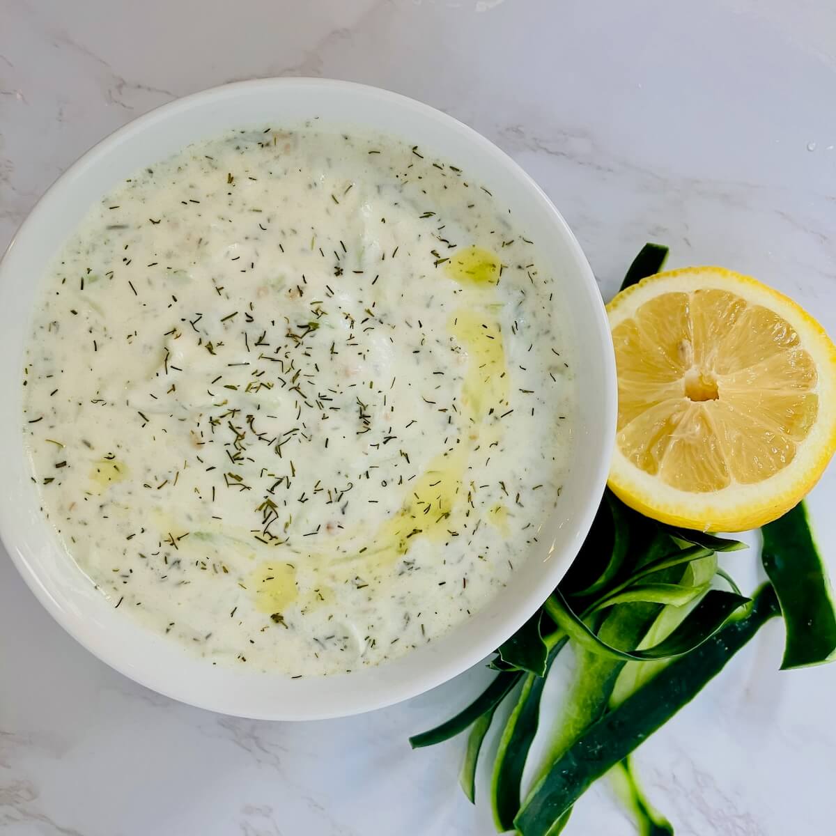 tzatziki sauce in a while bowl on a white background with a lemon and cucumber peel