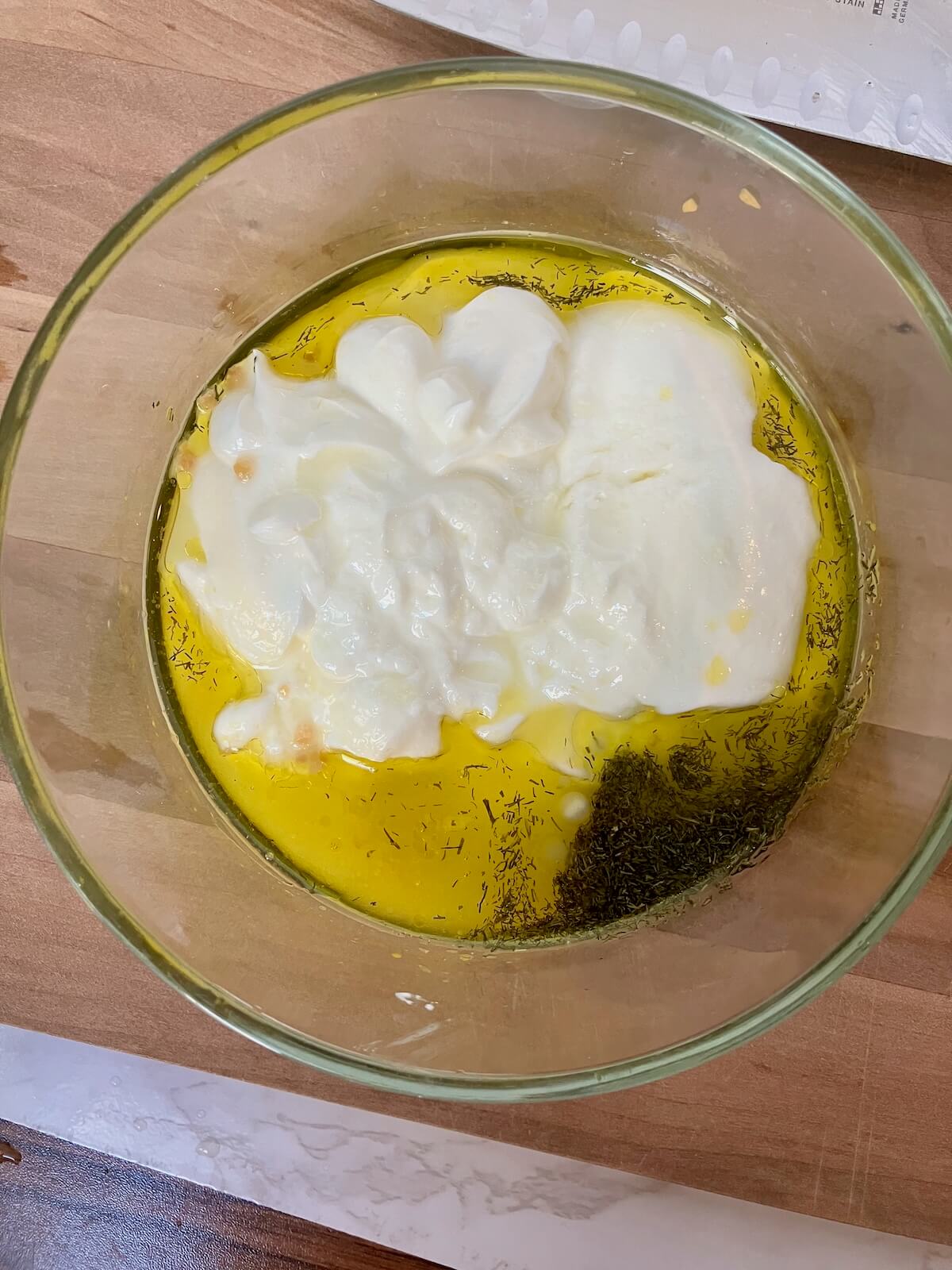 yogurt, olive oil and spices in a glass bowl on a wooden cutting board