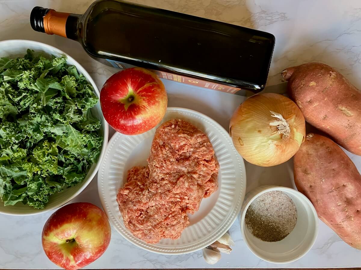 ingredients for sausage, apple and sweet potato bowl on a white marbled background