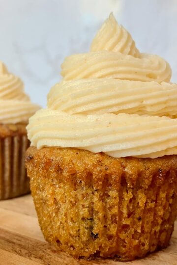 close up of a carrot cake cupcake with cream cheese frosting on a wooden cutting board with white background