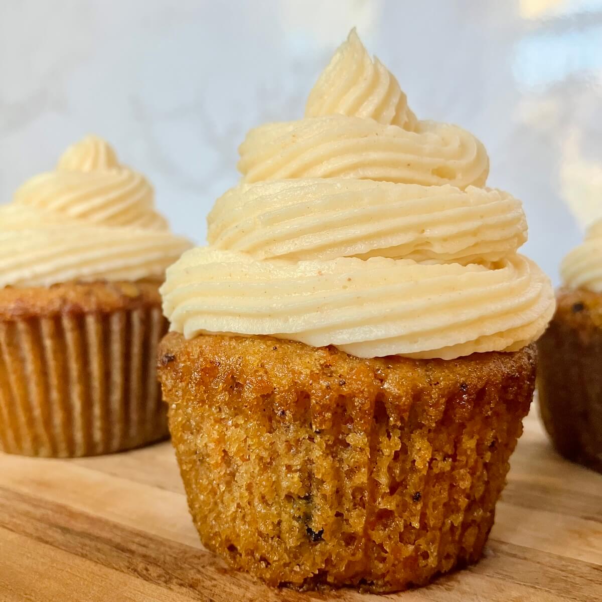 close up of a carrot cake cupcake with cream cheese frosting on a wooden cutting board with white background