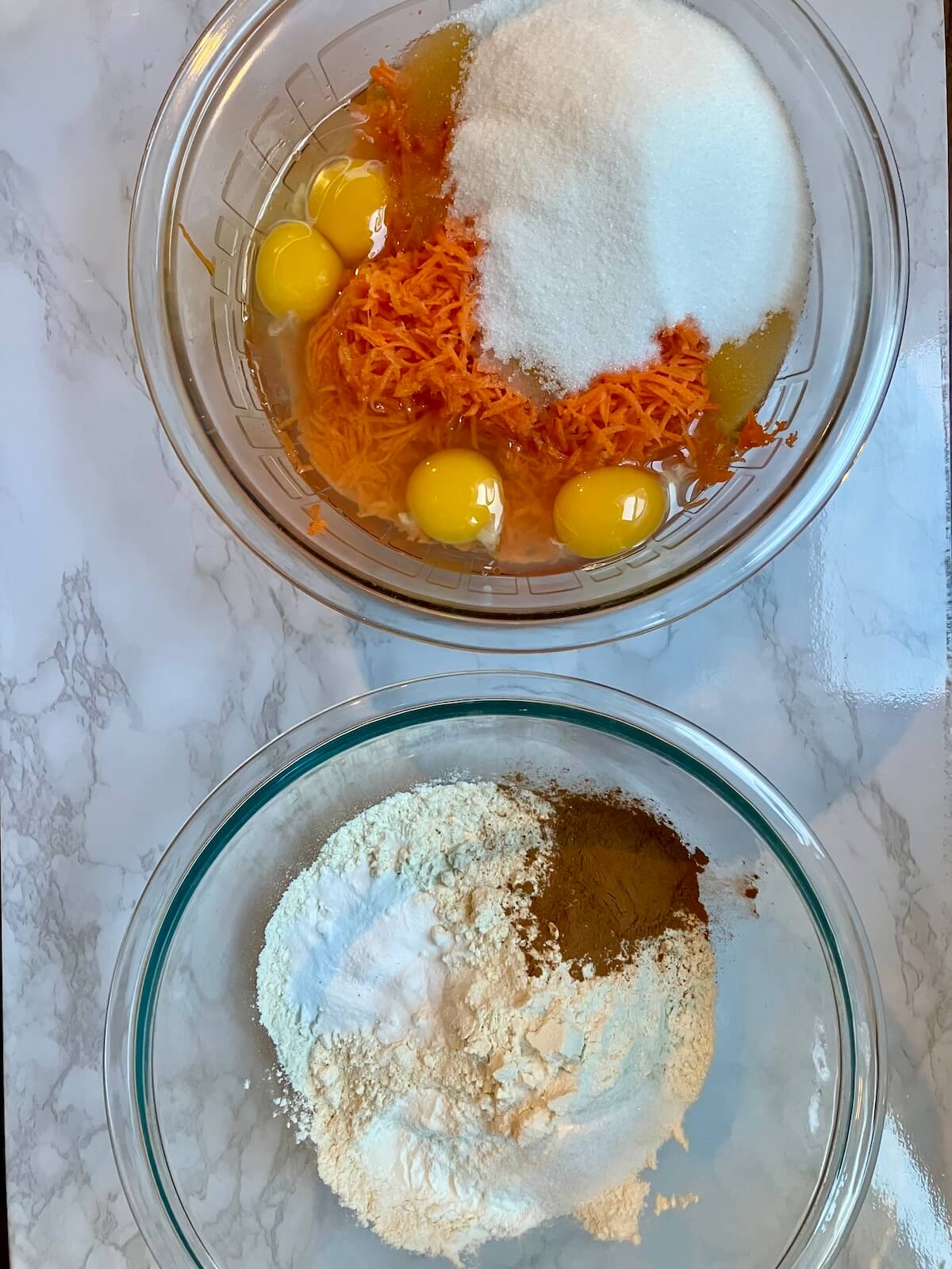 two glass bowls of carrot cake ingredients. one with dry ingredients one with wet ingredients