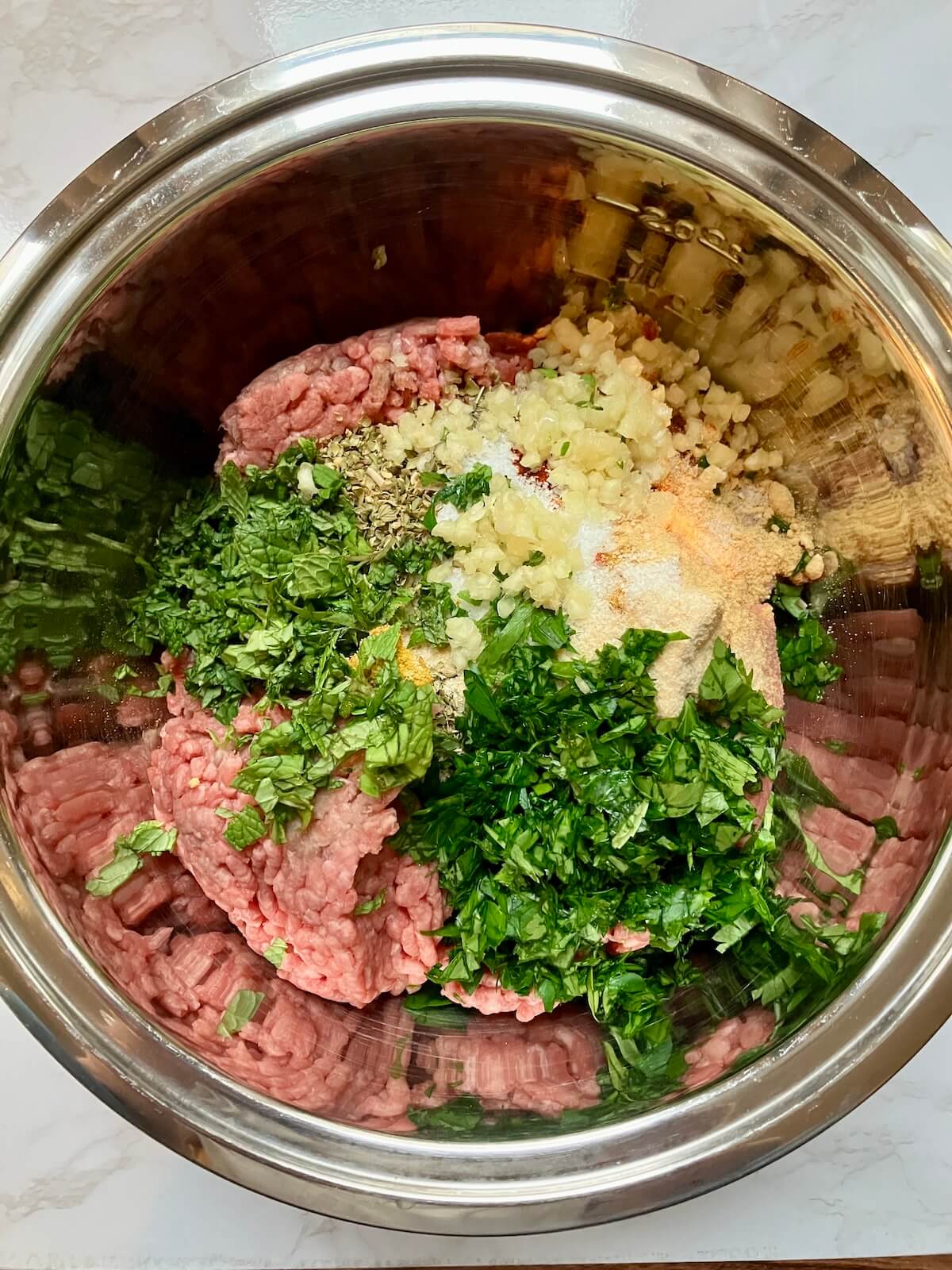beef kofta meat herbs and spices in a stainless steel bowl