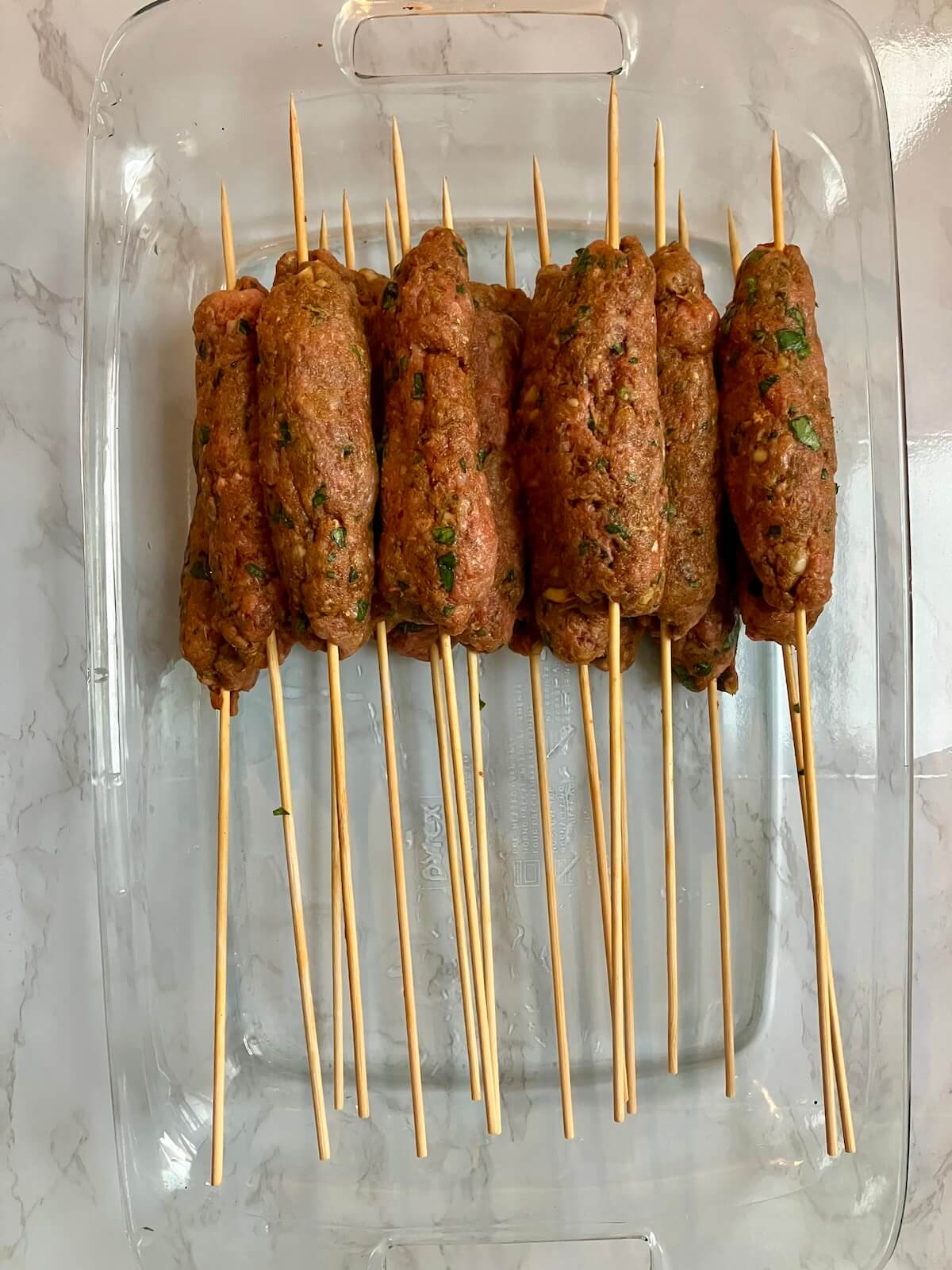 raw beef koftas on skewers in a glass dish