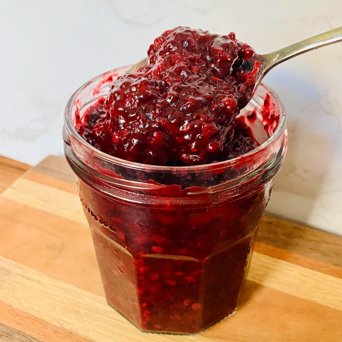 berry chia jam in a mason jar being scooped by a spoon
