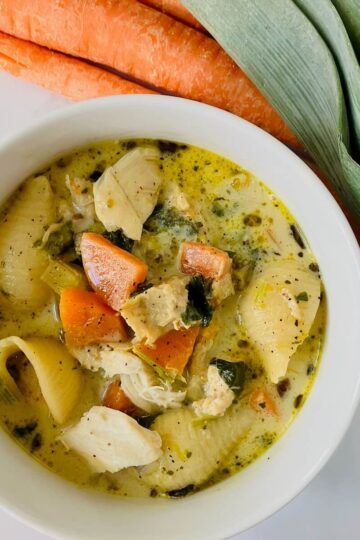 creamy chicken soup in a white bowl with carrots and leeks in the background
