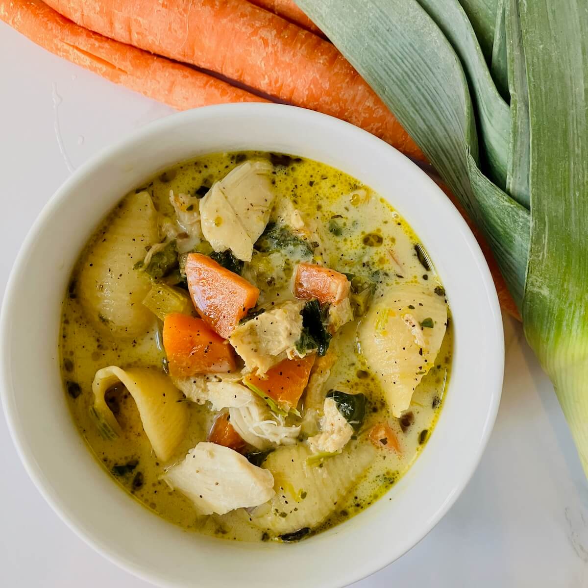 creamy chicken soup in a white bowl with carrots and leeks in the background