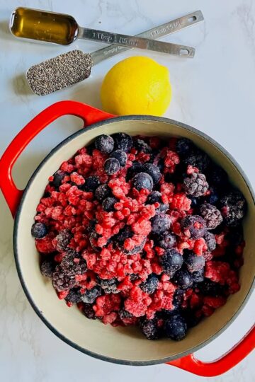 berries in a pot, a lemon and two measuring spoons with honey and chia seeds on a white marble background