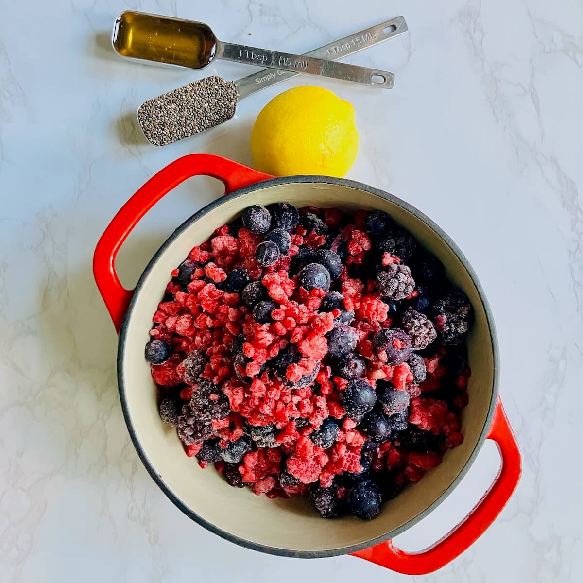 berries in a pot, a lemon and two measuring spoons with honey and chia seeds on a white marble background